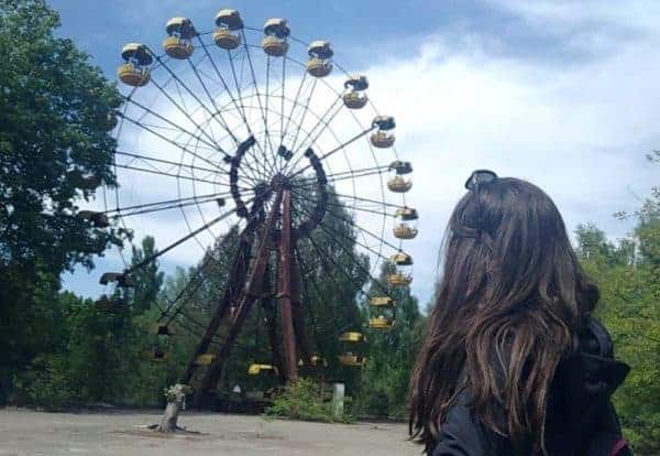 A woman observes a crumbling ferris wheel in Chernobyl's deserted amusement park