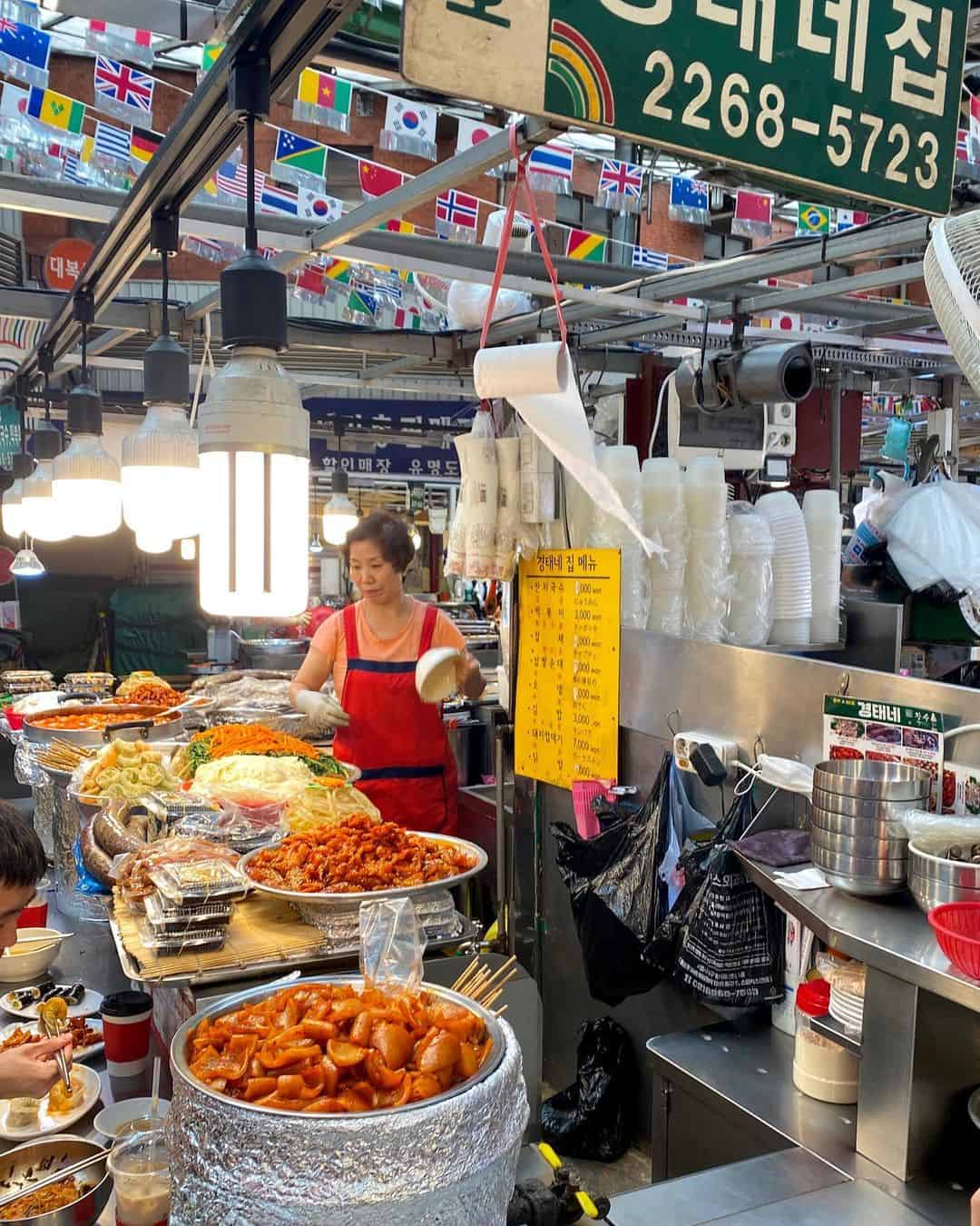 A woman poses in front of a bustling food stand at Gwangjang Market