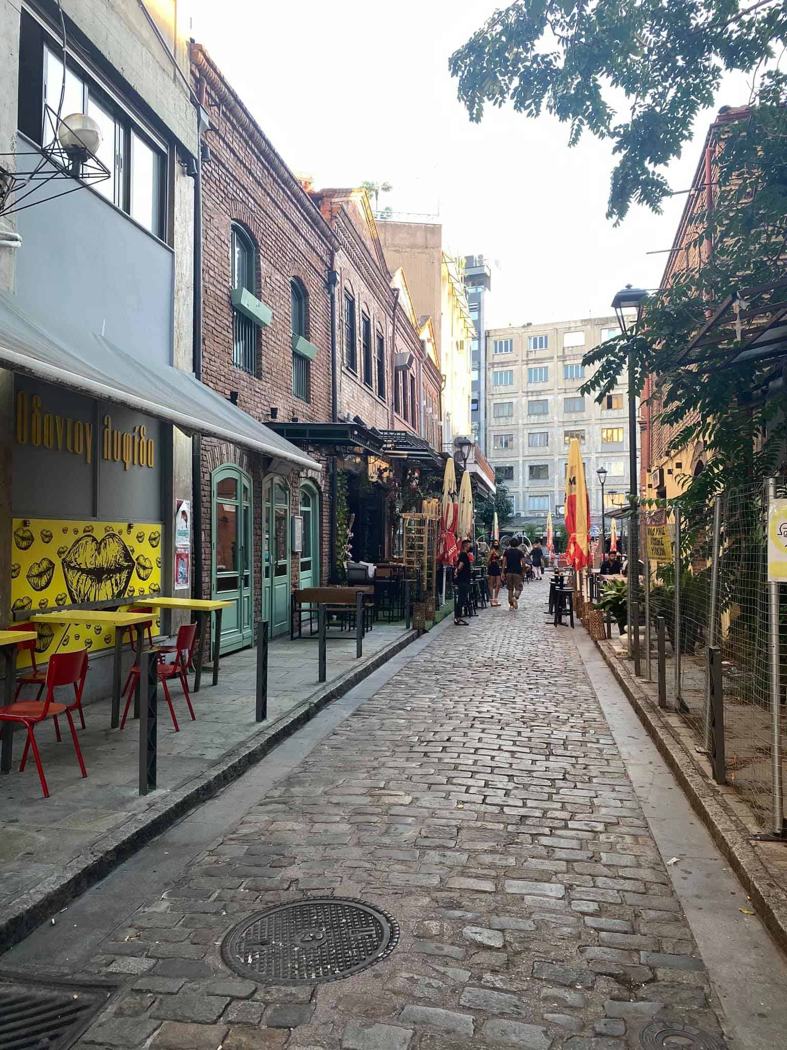 A narrow cobblestone street lined with outdoor tables and chairs