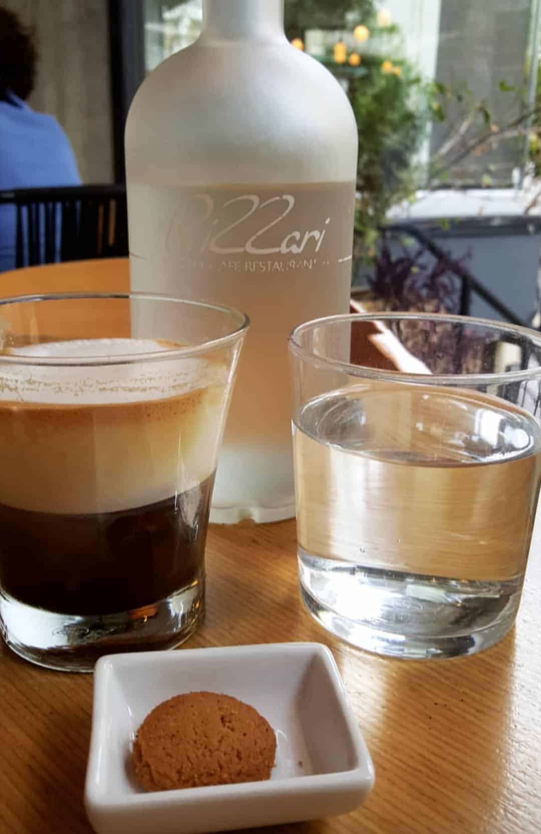 A glass of coffee beside a cookie placed on a wooden table