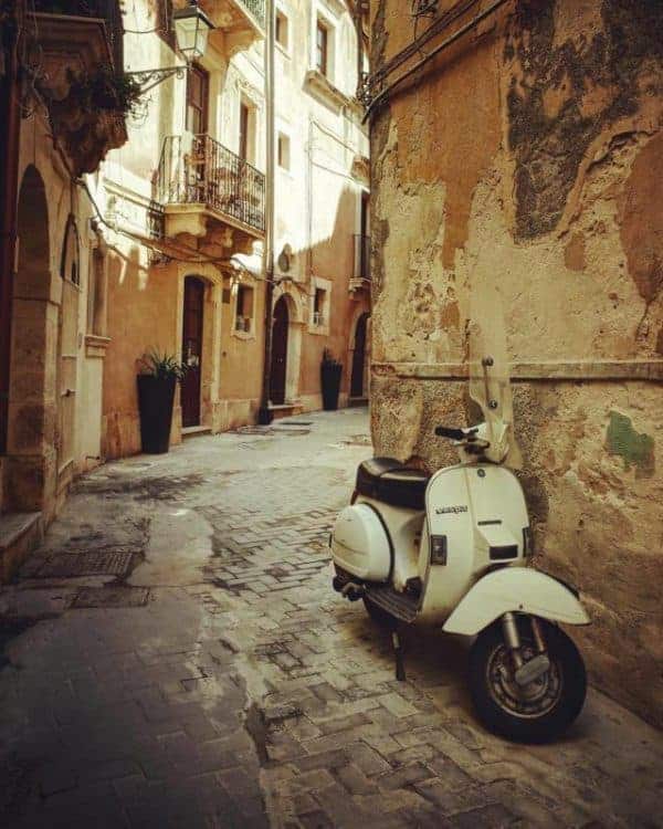 A vibrant Vespa scooter stands parked in a quaint alleyway