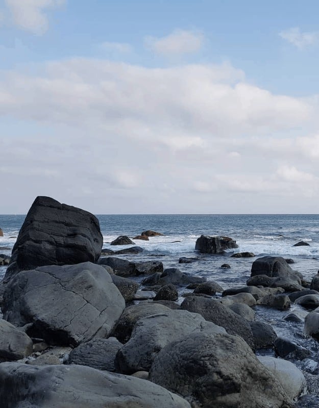 A scenic rocky beach featuring large boulders surrounded by gentle waves lapping at the shore