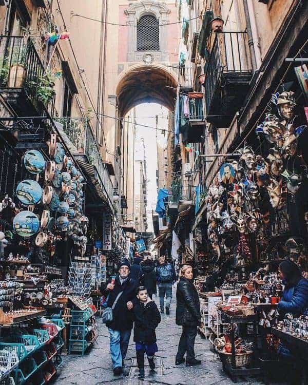 A narrow alley in Naples bustling with people walking through