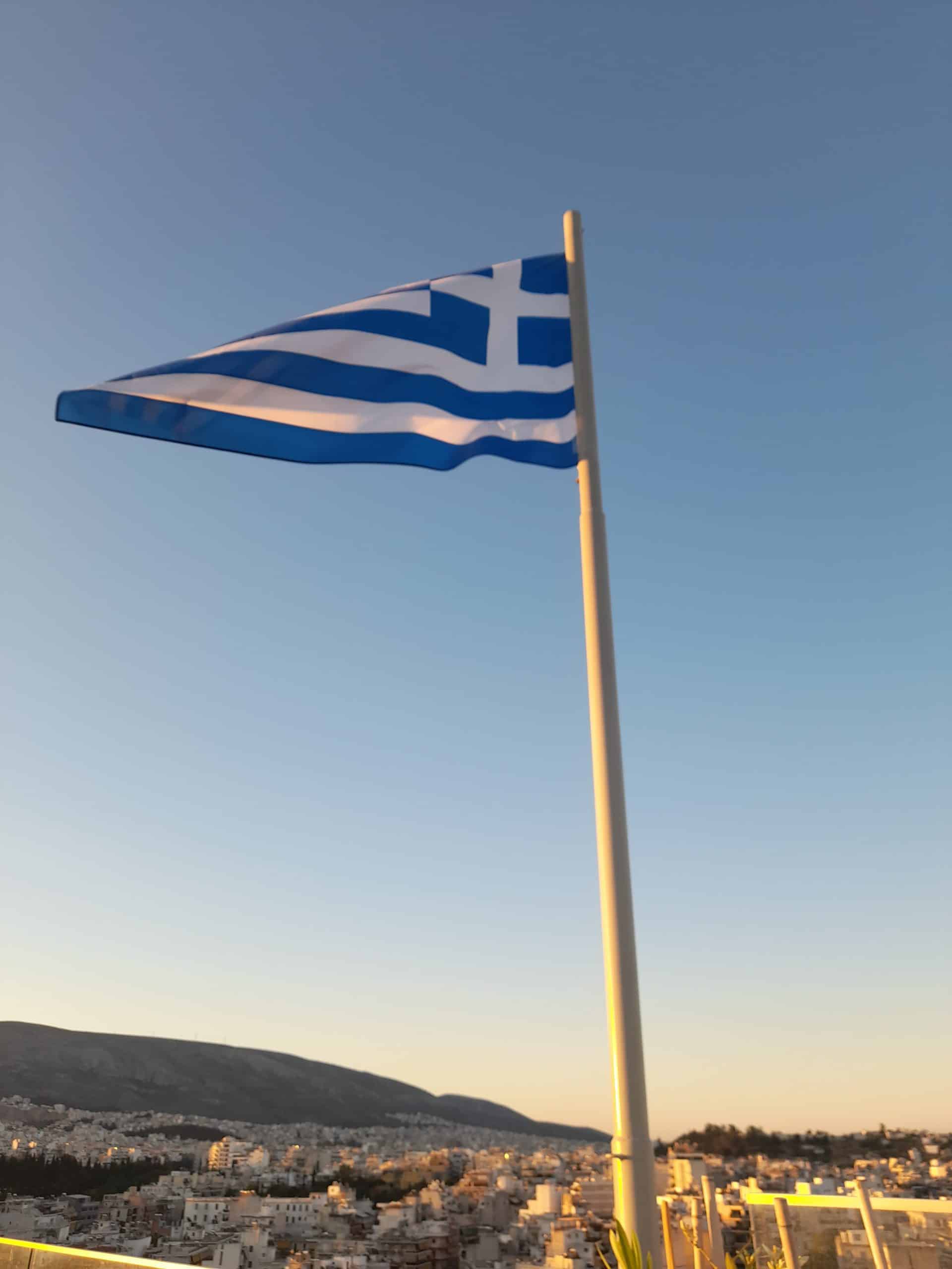 The flag of Greece proudly waves against a clear blue sky