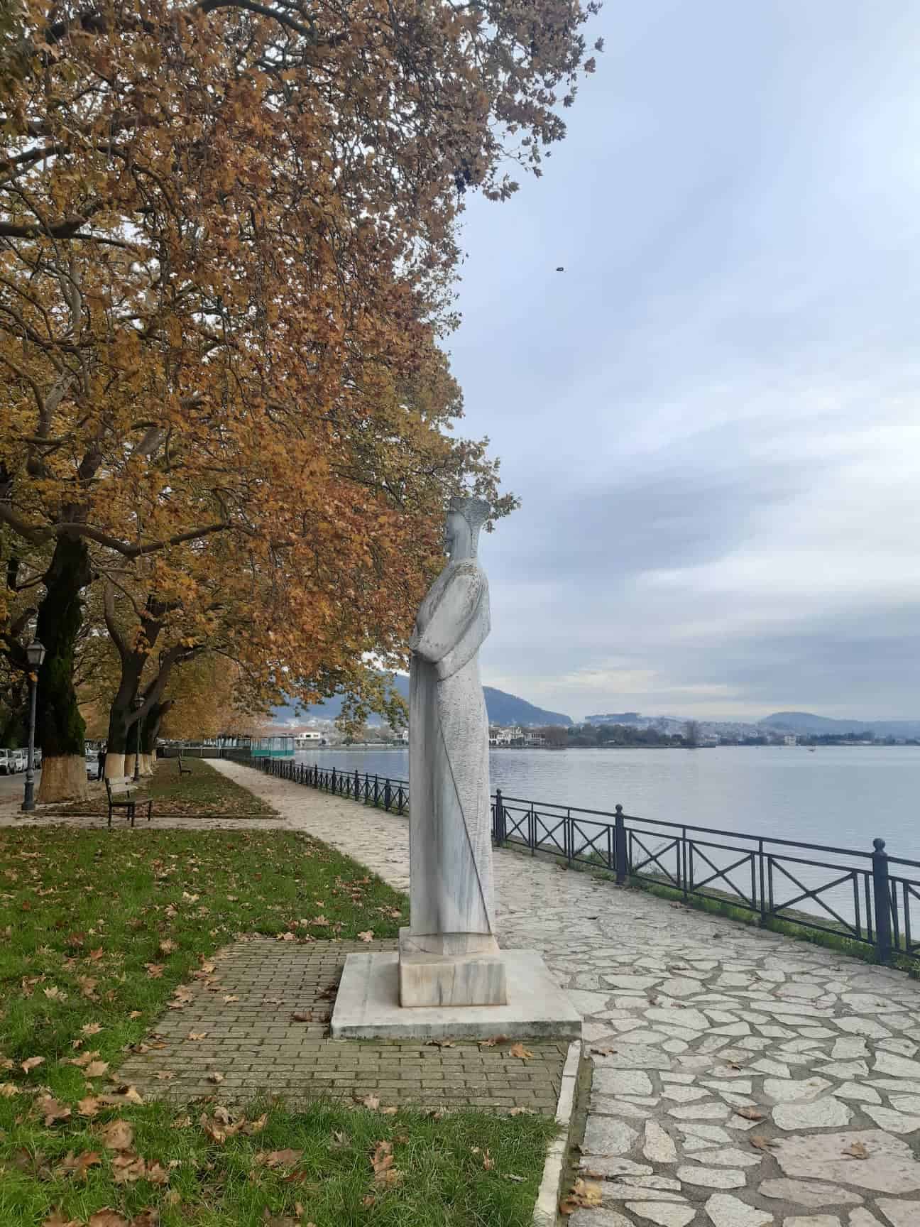 A statue of a woman stands gracefully on a path beside the water