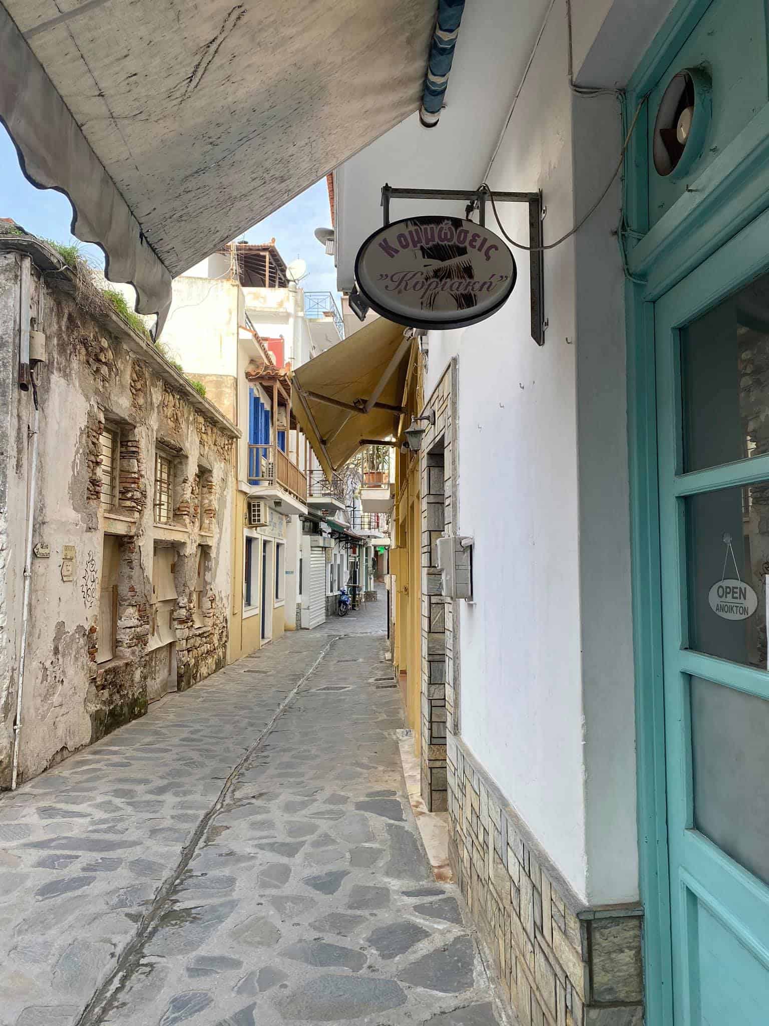 A narrow street in Greece featuring a vibrant blue door and a decorative sign