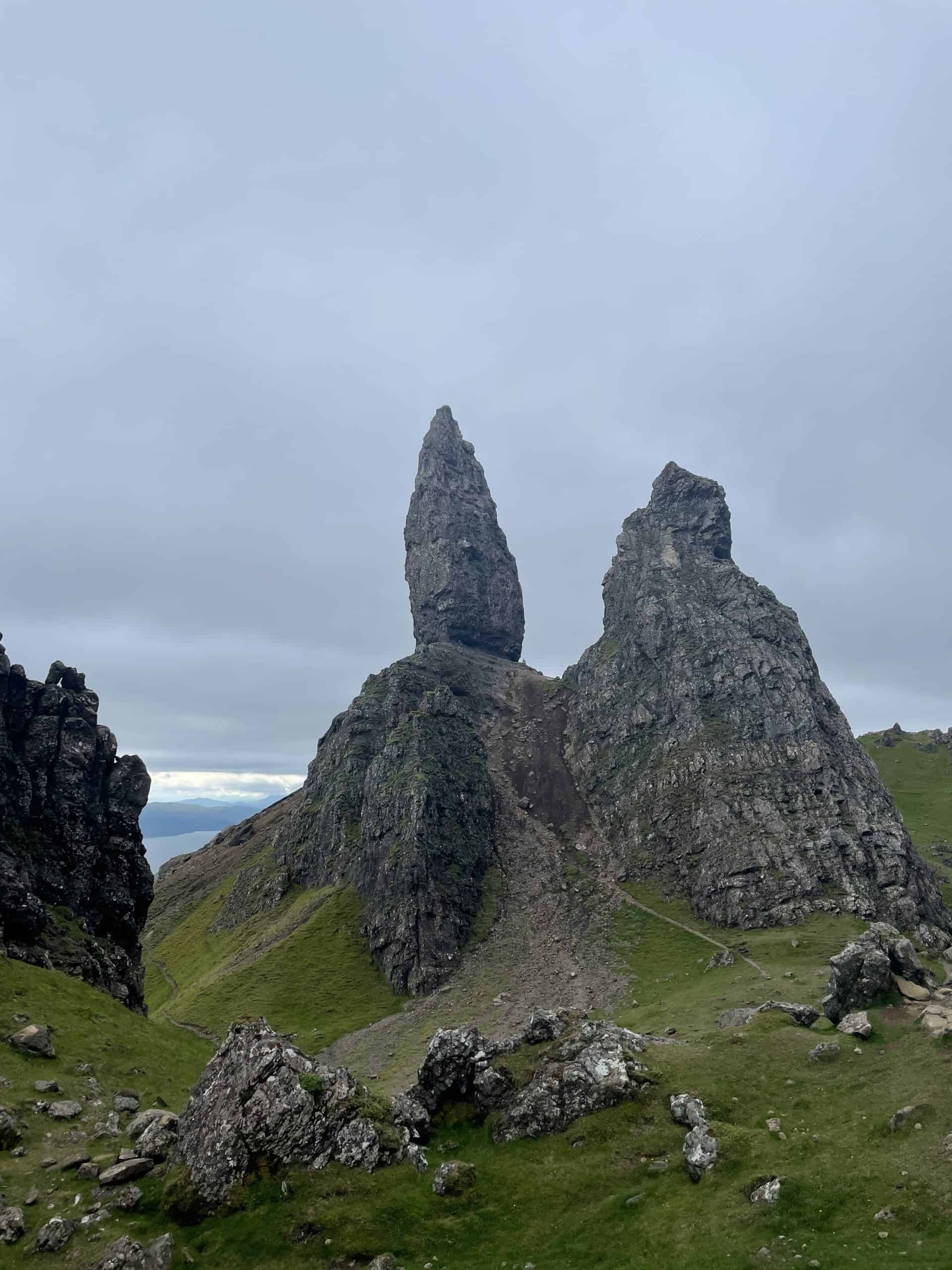 The iconic Old Man of Storr rises prominently against a backdrop of rolling hills and a cloudy sky