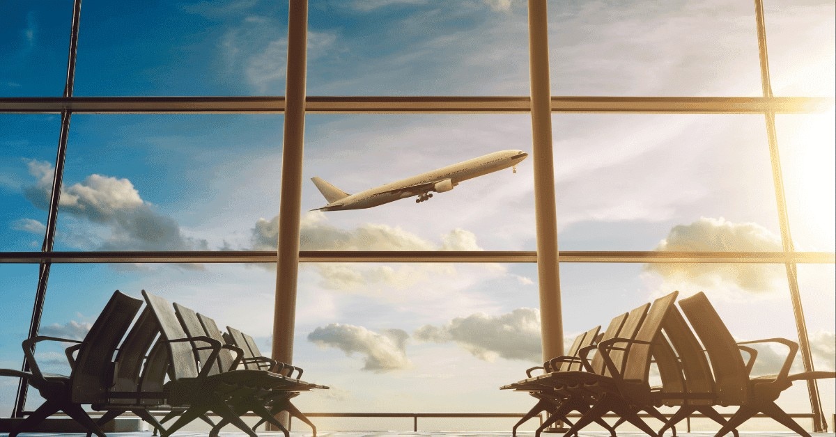 An airplane soars above a window featuring several chairs