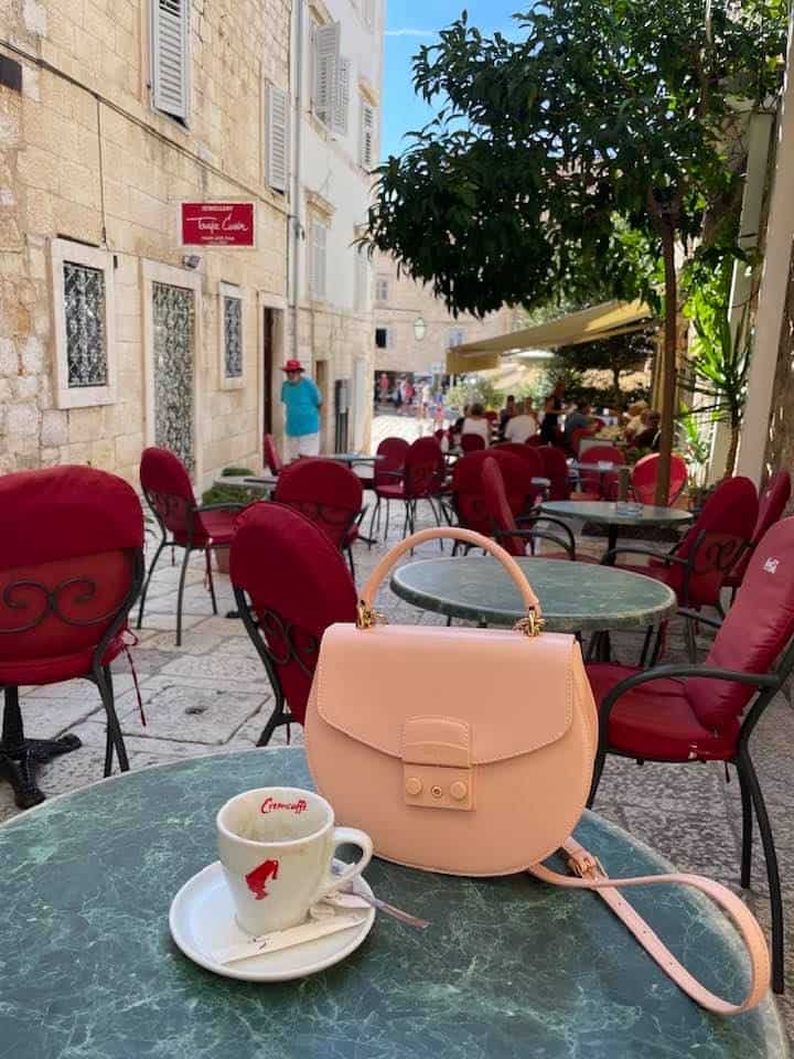 A pink purse and a coffee cup are placed on a table outdoors