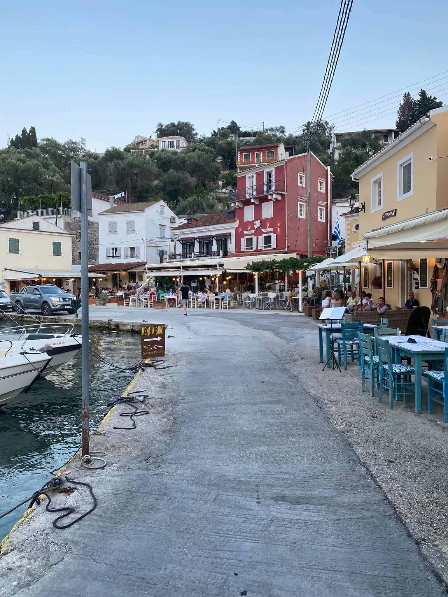 A marina scene featuring boats docked alongside tables set in front of a building