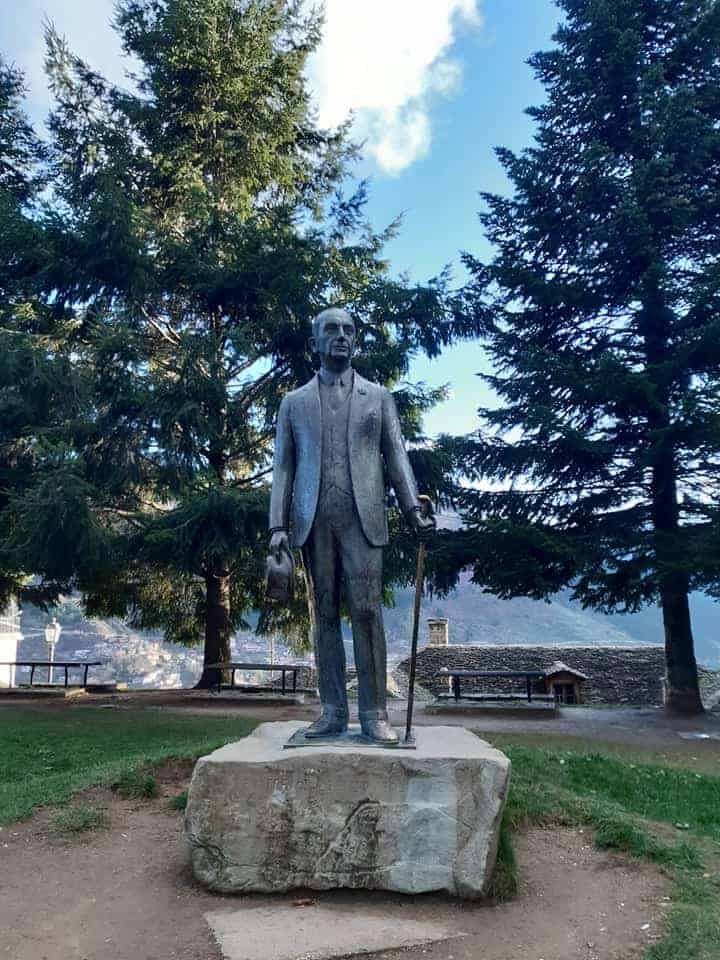 A statue of a man stands prominently in front of lush green trees