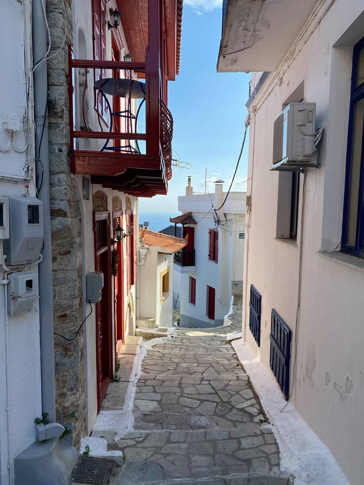 A narrow street characterized by white buildings and bright red balconies