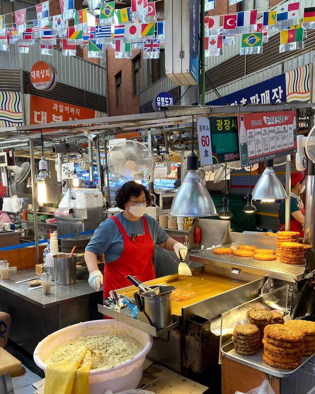 A woman in an apron skillfully prepares food at a bustling market