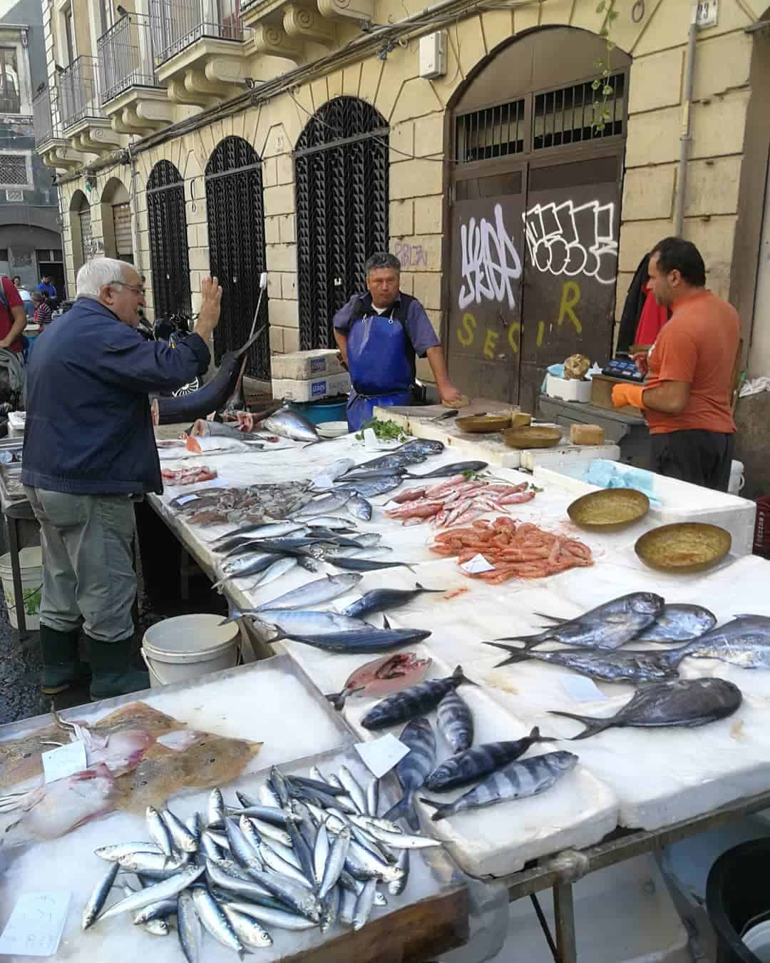 A man stands before a table displaying various types of fish