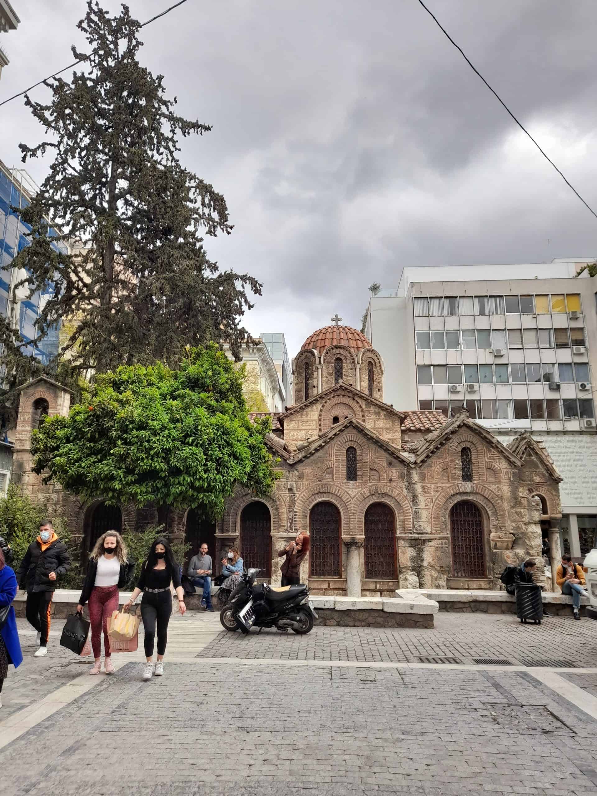 Individuals walk leisurely around a small church located amidst the urban landscape of the city