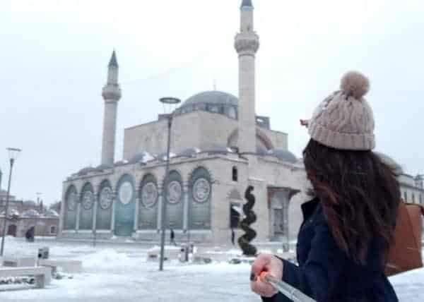 Woman walks in the snowy landscape near a mosque in Turkey