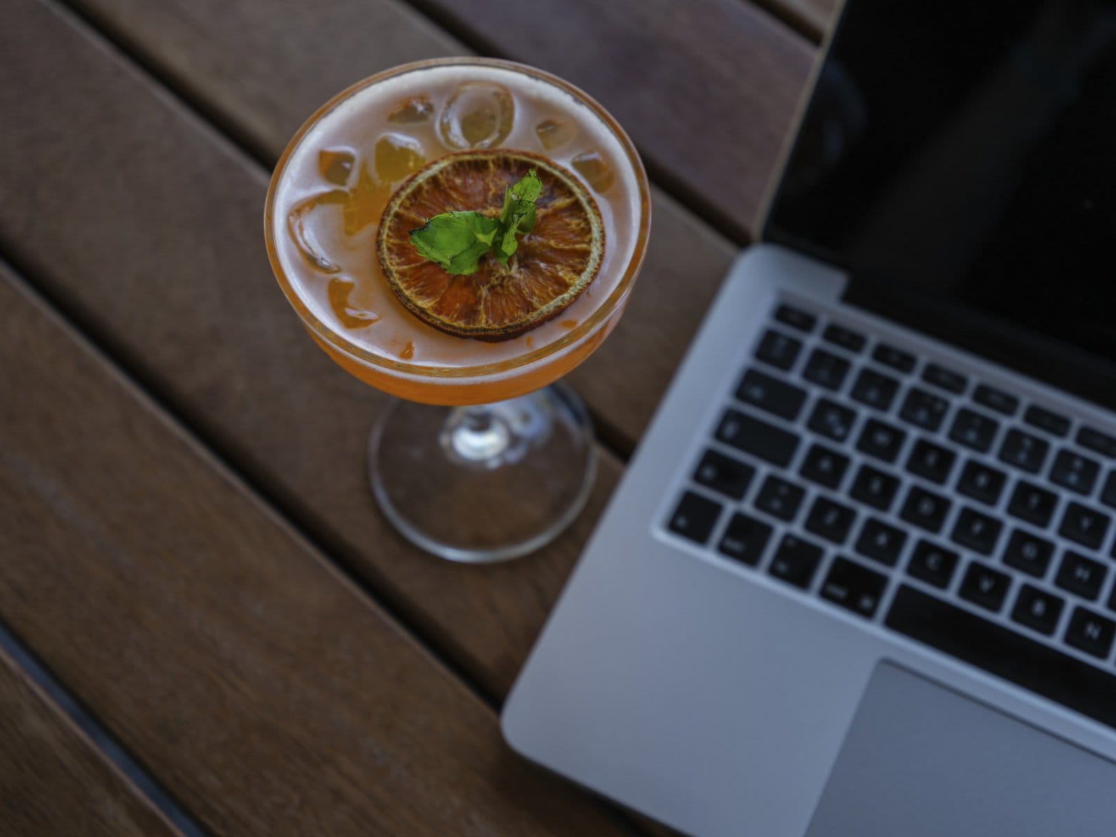 A glass of orange drink placed beside a laptop on a wooden table