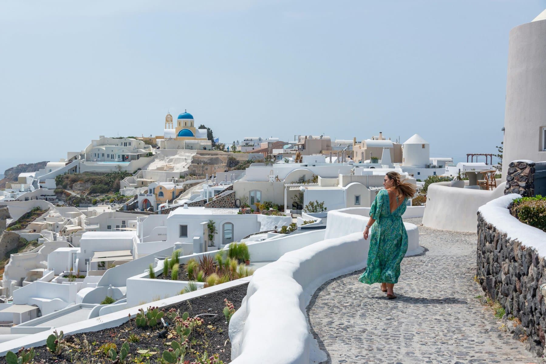 A woman in a green dress strolls along a path beside a white building