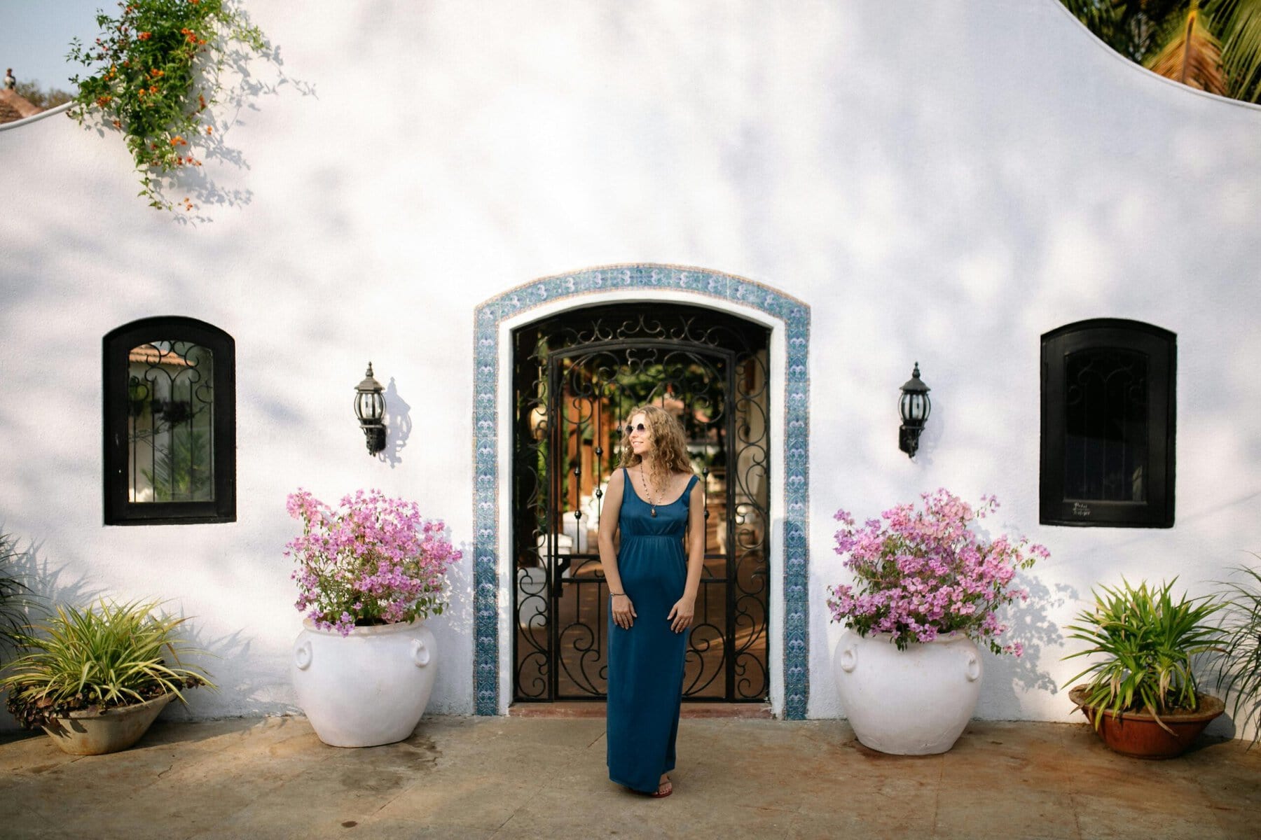 A woman in a blue dress stands gracefully in front of a charming white house