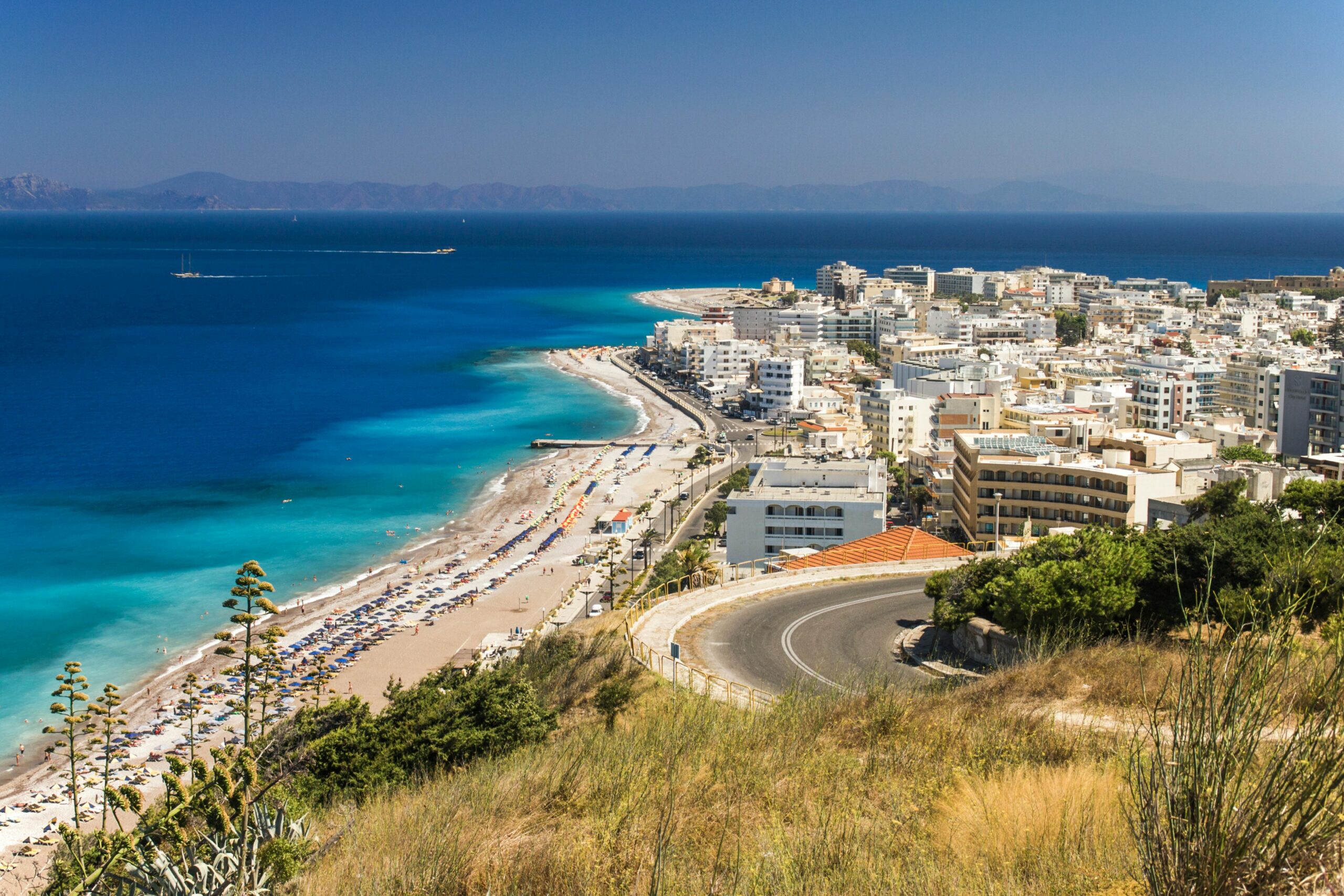 A serene beach view featuring soft sand and vibrant blue water under a clear sky