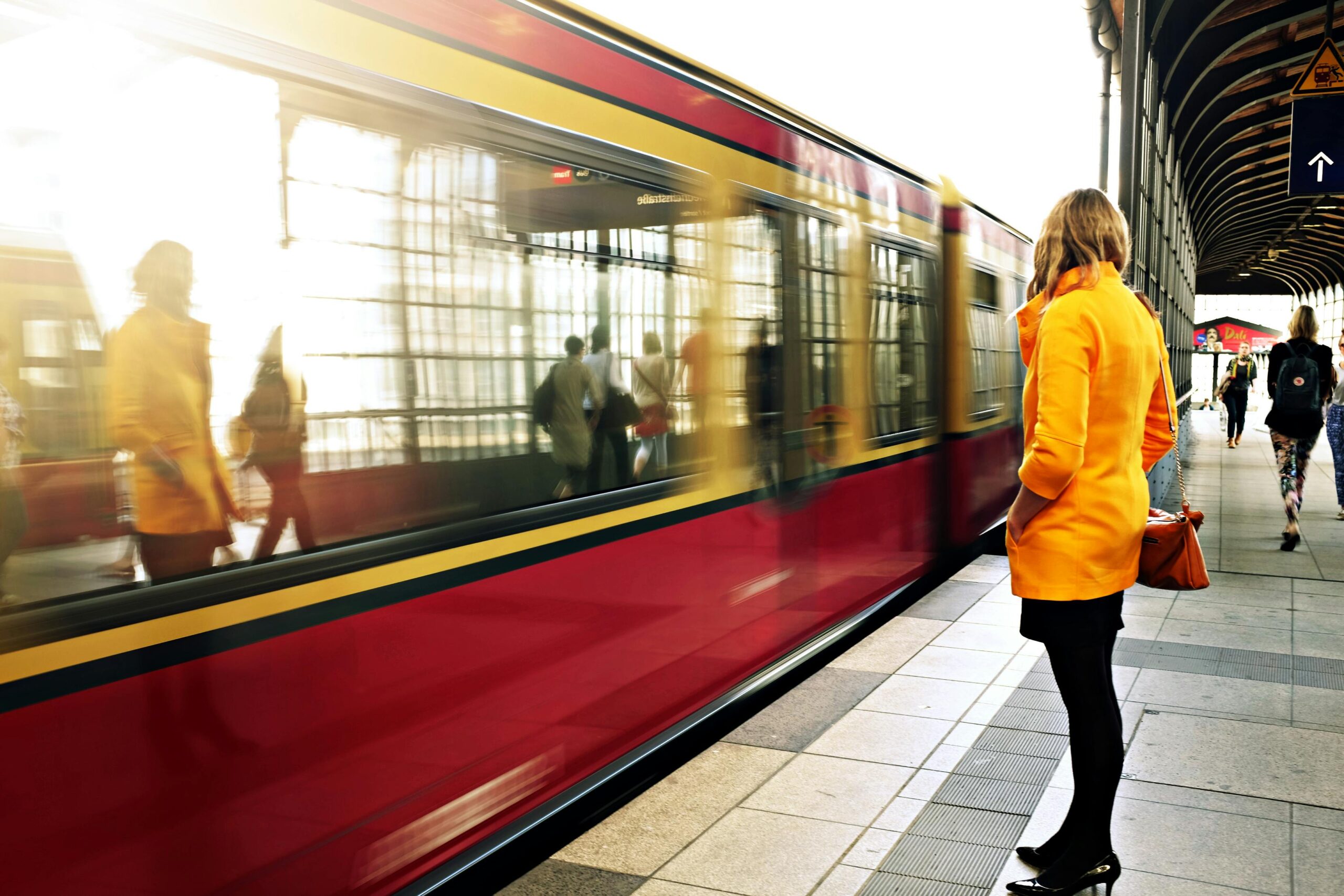 A woman in a yellow coat stands beside a train