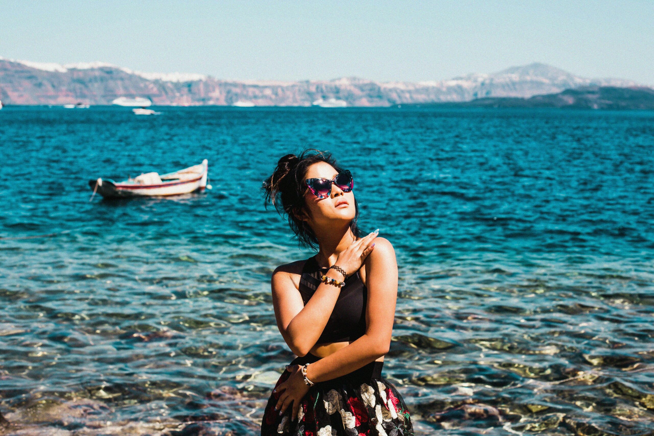 A woman wearing sunglasses stands on the shore of a serene lake