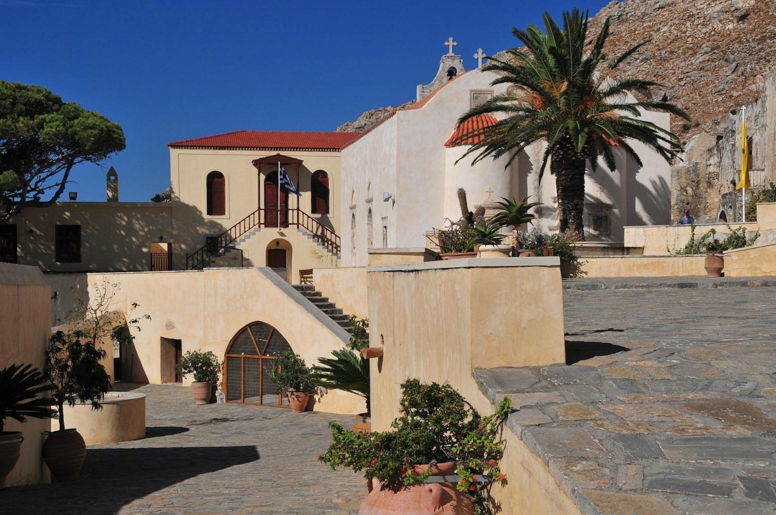 A church featuring a red roof stands beside a tall palm tree against a clear blue sky