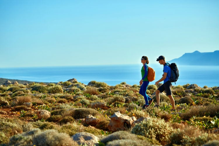 Two individuals with backpacks traverse a rocky hillside