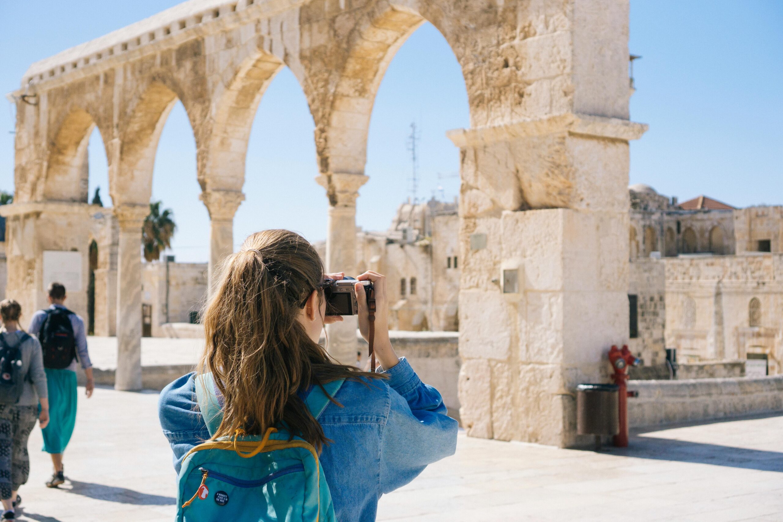 A woman capturing a photograph of the historic skyline of Jerusalem, showcasing its ancient architecture and vibrant atmosphere