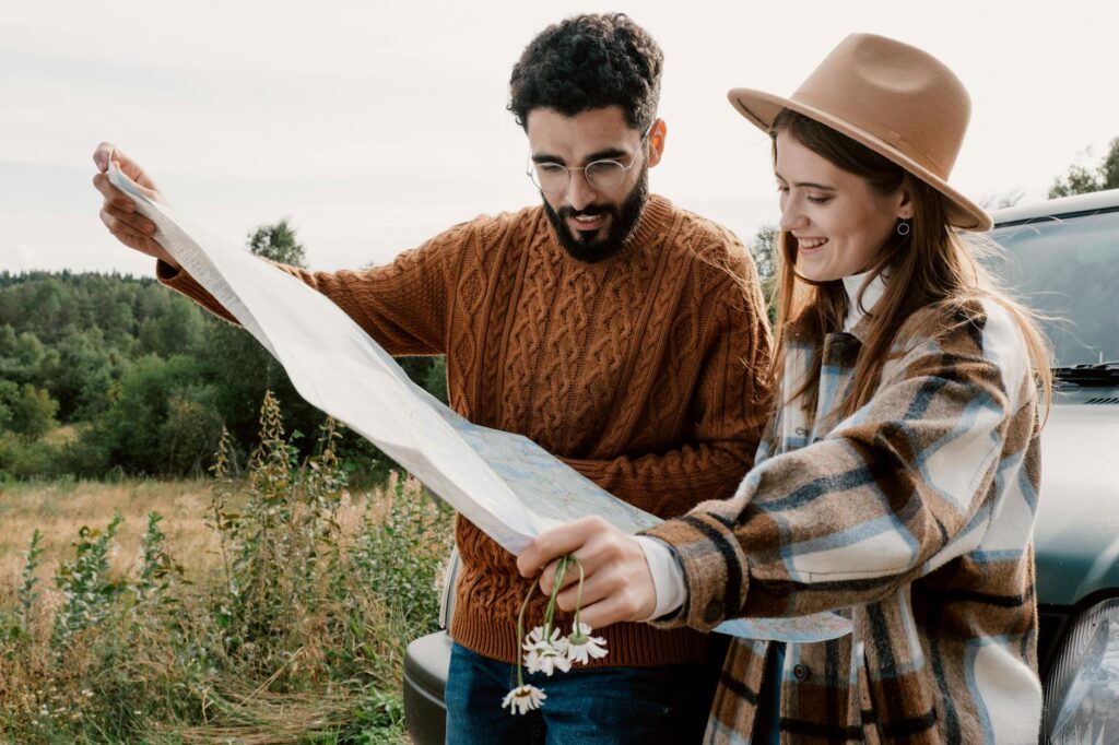 A couple dressed warmly, studying a map together outdoors, set against a serene natural backdrop, planning their travel adventure.