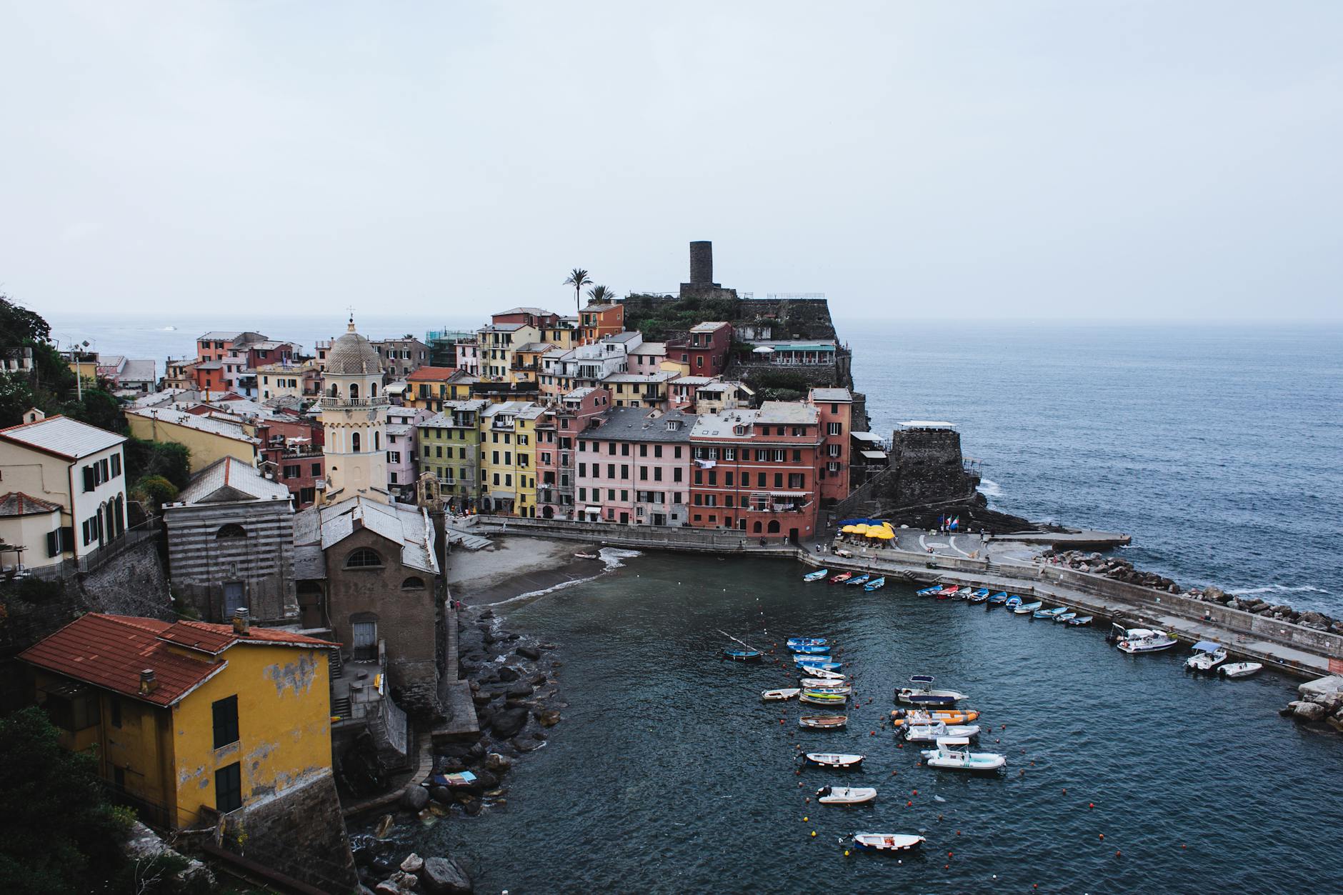 Aerial view of a small coastal town with colorful buildings, boats floating near a pier, and serene sea waters, capturing small-town travel charm and natural beauty.