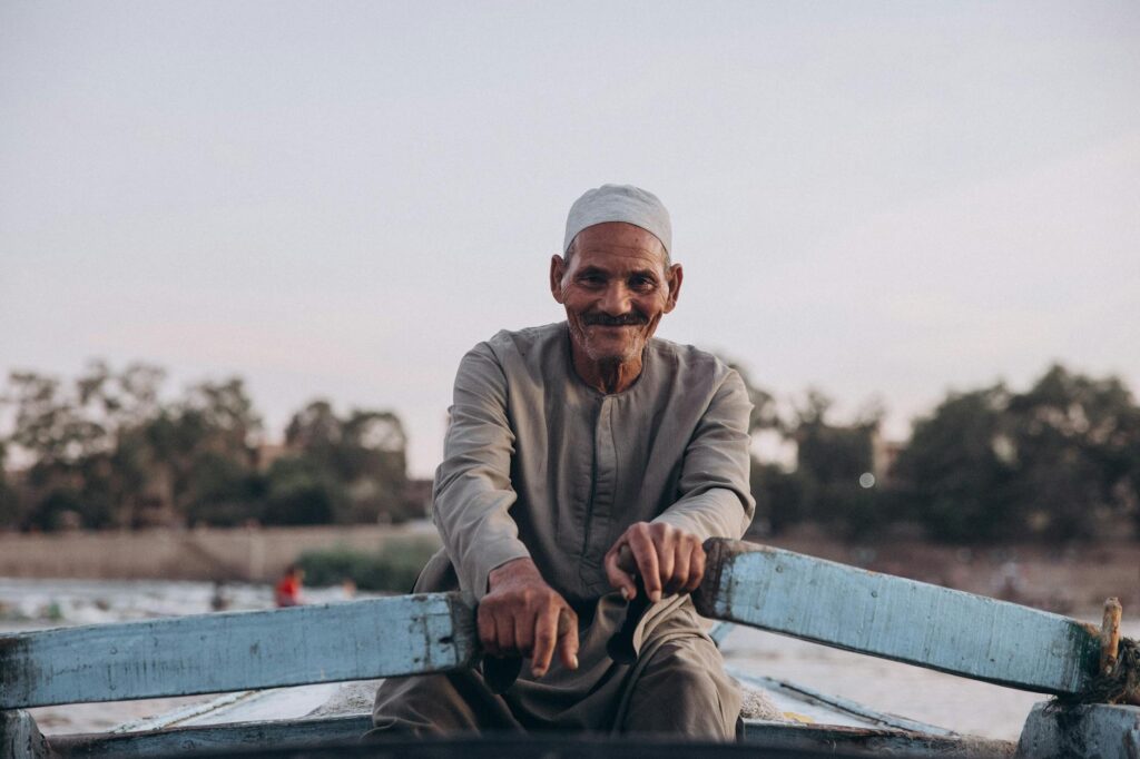 An elderly man enjoys a peaceful boat ride on the Nile River, surrounded by calm waters and natural beauty in Al Qanatir, Egypt