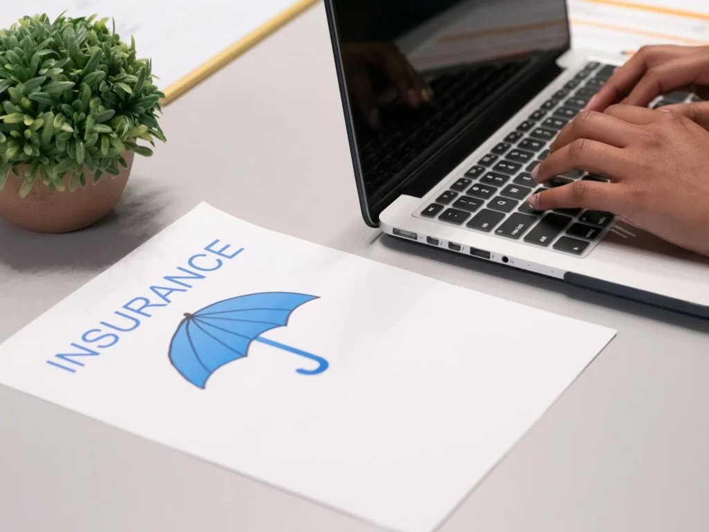 Close-up of hands typing on a laptop with an insurance document on the desk, representing travel insurance planning and research.