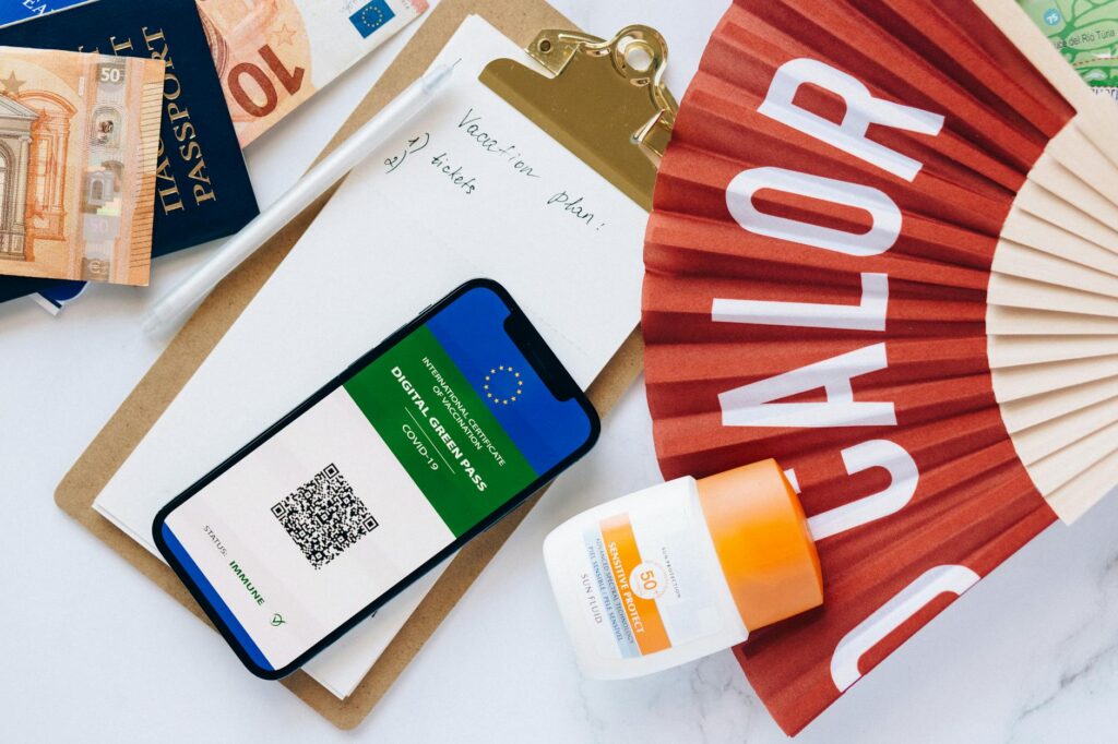 Flat lay of travel essentials including a passport, digital green pass, and boarding pass, emphasizing travel preparation and safety