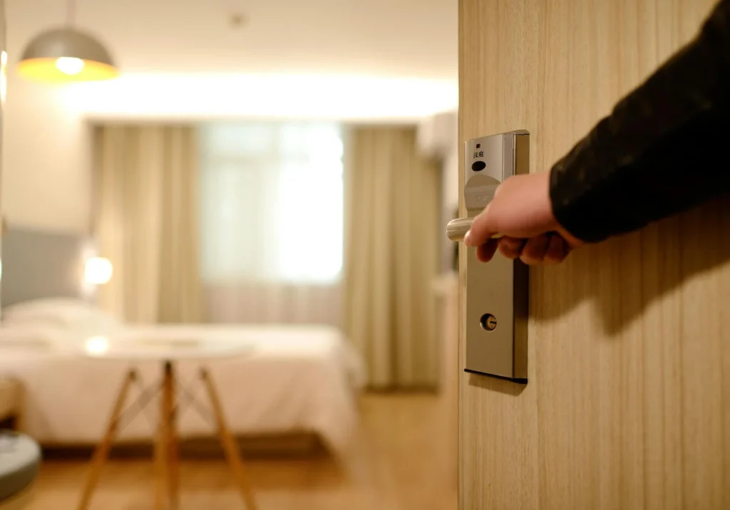 Hand opening a hotel room door to a cozy, bright interior, ideal for slow travel accommodations