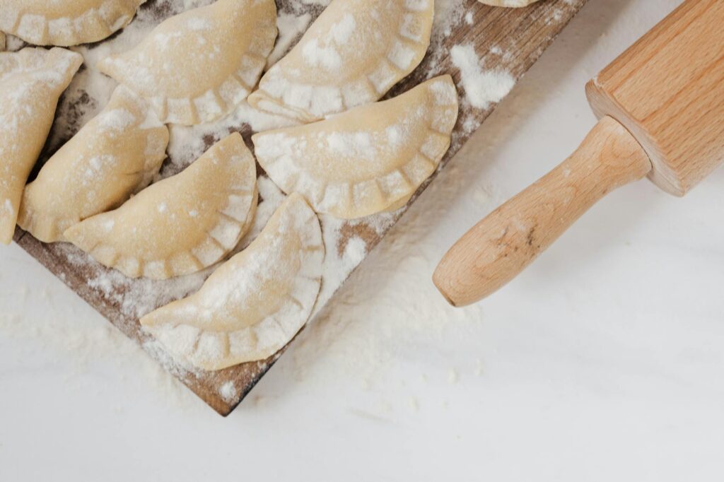 Handmade pierogi on a floured wooden board with a rolling pin, showcasing traditional Eastern European dumpling preparation