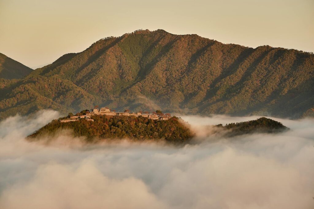 Misty autumn morning enveloping a historic castle surrounded by lush, colorful mountain scenery.