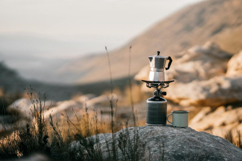 Outdoor coffee brewing with a portable stove against a scenic mountain backdrop, ideal for slow travel and nature exploration