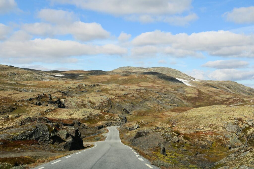 Scenic autumn road winding through rugged Norwegian mountains under a bright, clear sky.