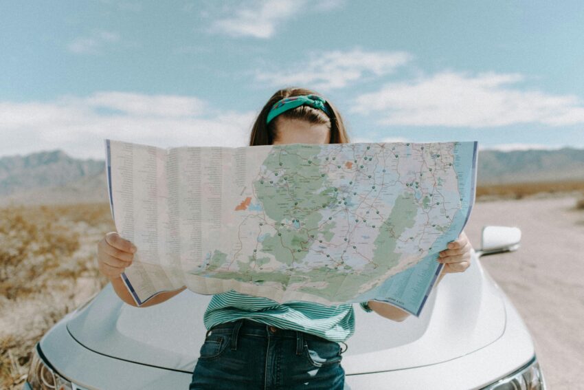 Traveler holding a map by a car in a scenic desert, symbolizing road trips, navigation, and outdoor exploration.