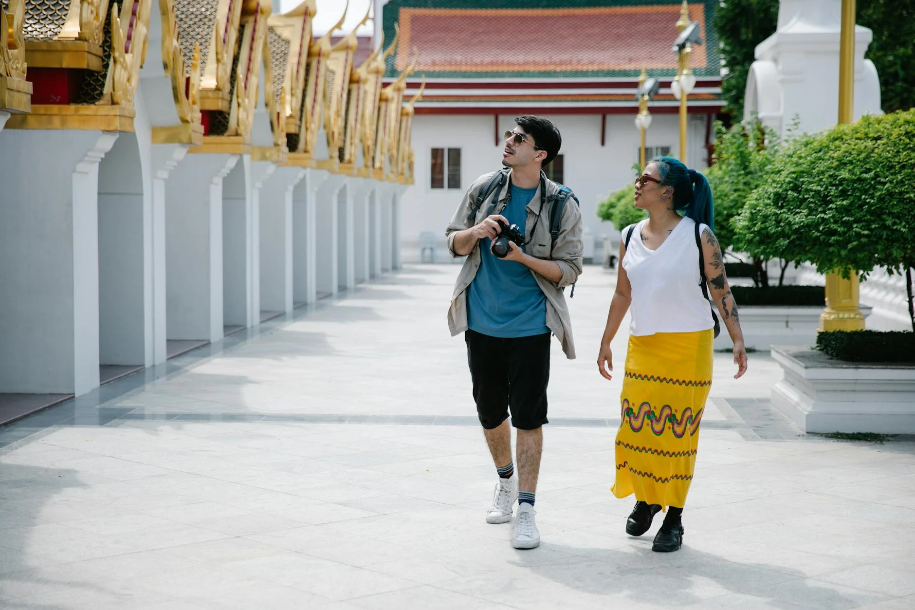 Two tourists walk and explore a traditional Thai temple, enjoying sightseeing and photography