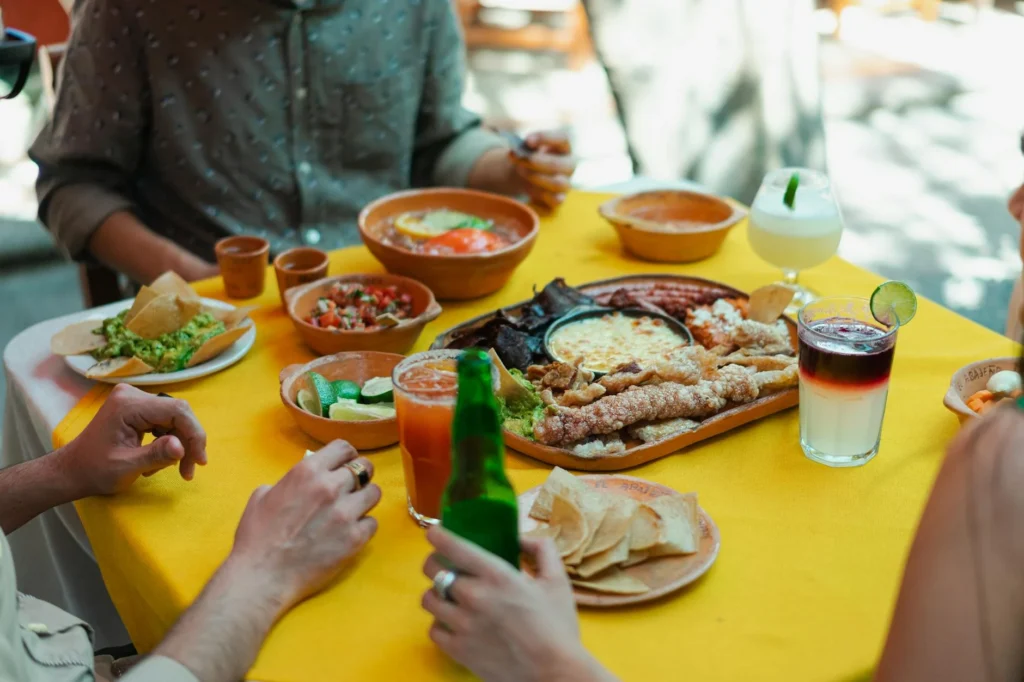 Vibrant outdoor dining scene with colorful Mexican dishes, refreshing drinks, and people enjoying meals in a festive atmosphere