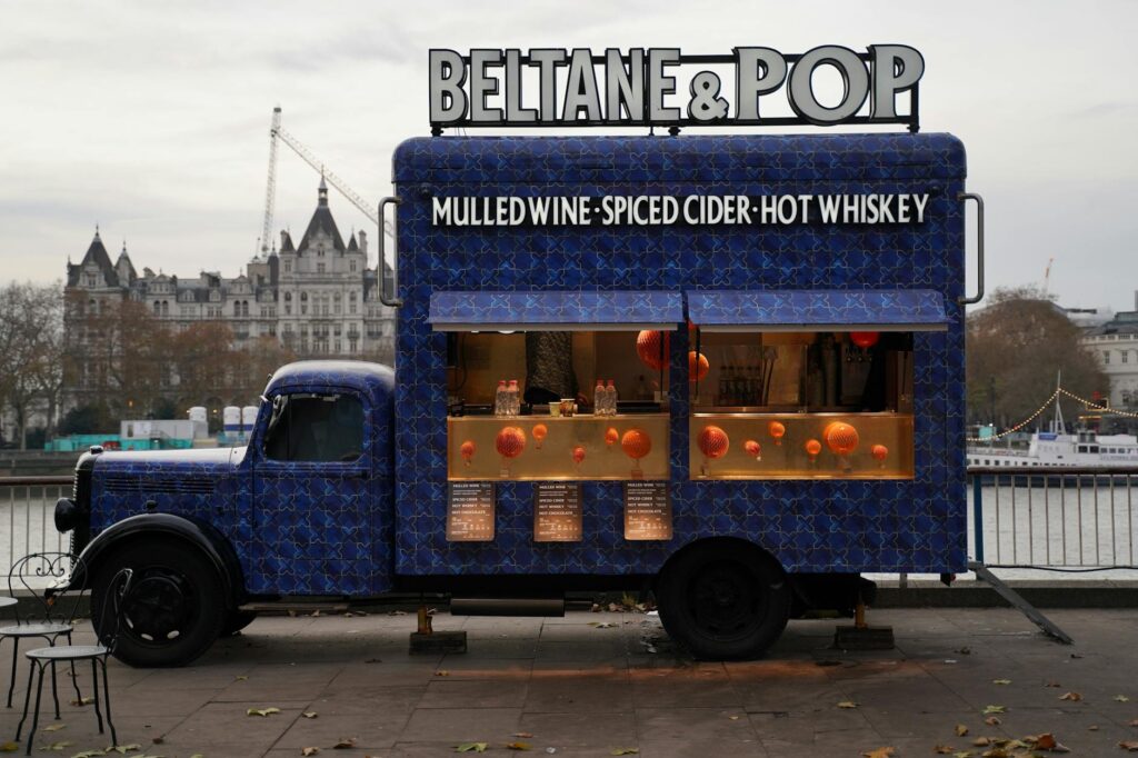 cozy riverside food truck serving mulled wine and spiced cider with a cityscape backdrop on a crisp autumn day