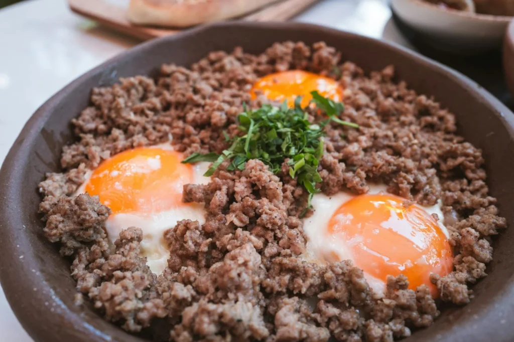 skillet breakfast with sunny-side-up eggs, seasoned ground beef, and fresh herbs, served in a rustic, homestyle presentation