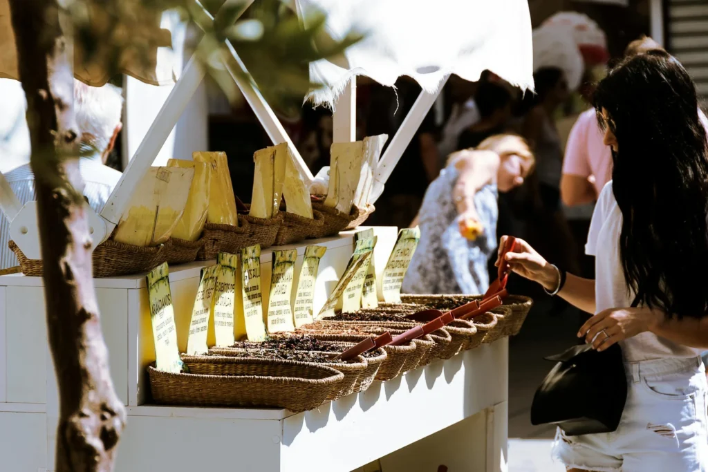 A lively street market scene with baskets of spices and people browsing on a sunny day.