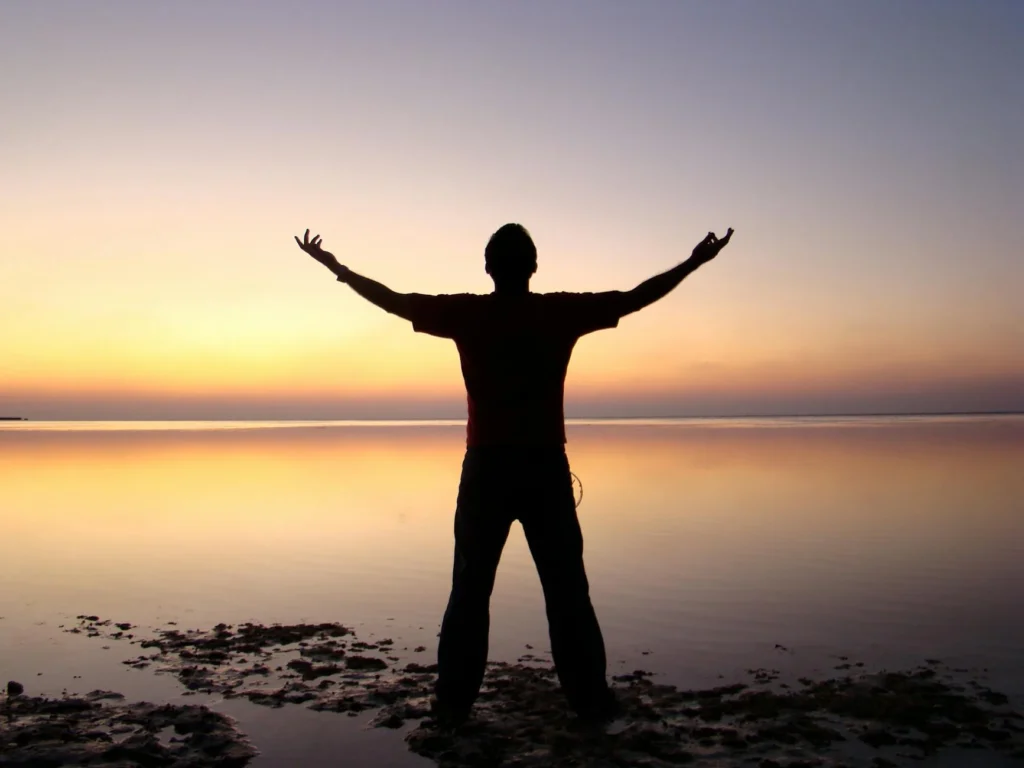 A person joyfully embracing the sunrise over a calm ocean, symbolizing freedom and solitude.