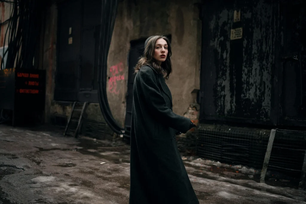 A woman in a coat walks through a grungy urban alley at night, exuding mystery.