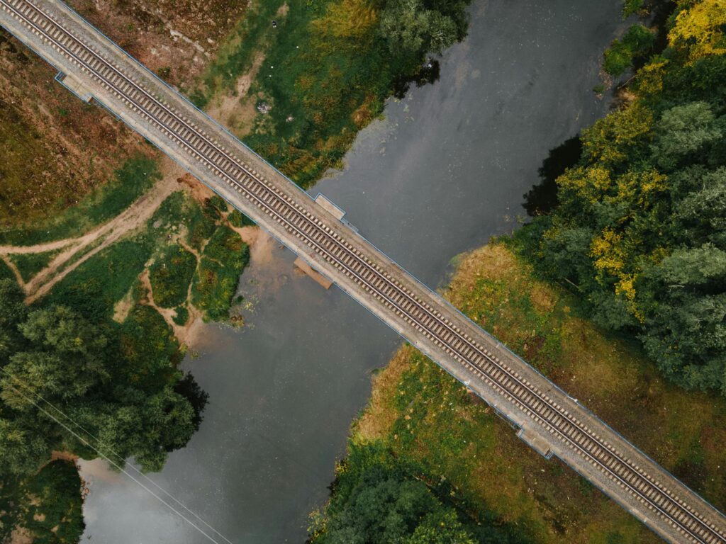 An aerial shot capturing a railway bridge crossing over a river in a lush, rural setting.