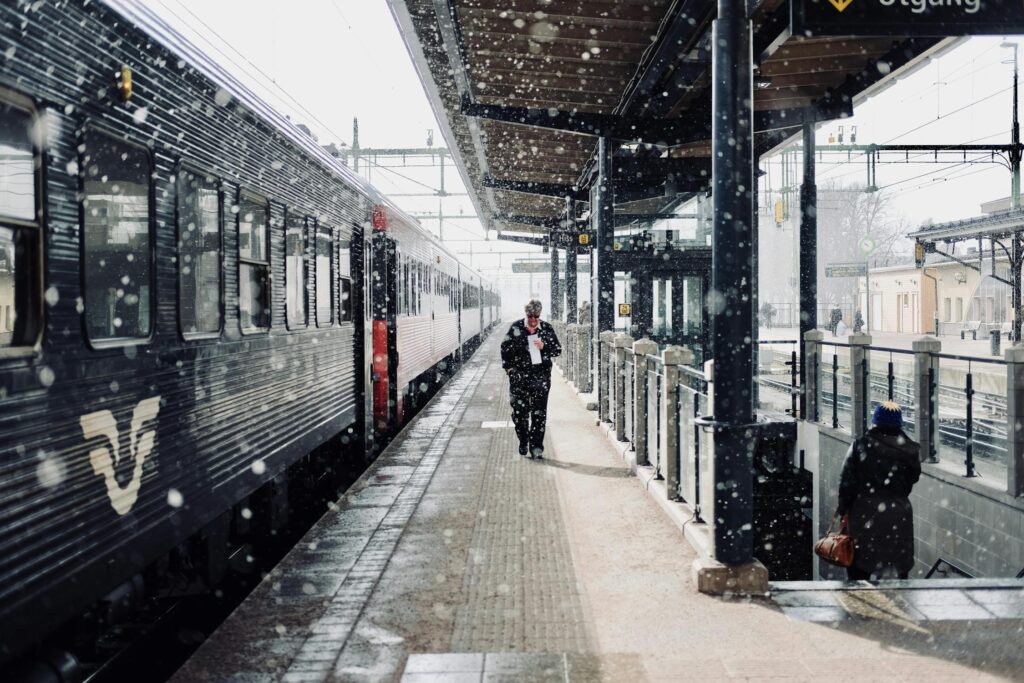 Commuters navigate a snowy platform at a train station in Sweden.