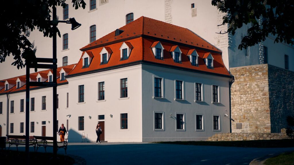 Front view of Bratislava Castle facade with vibrant red roof and clear blue sky, in sunlight.